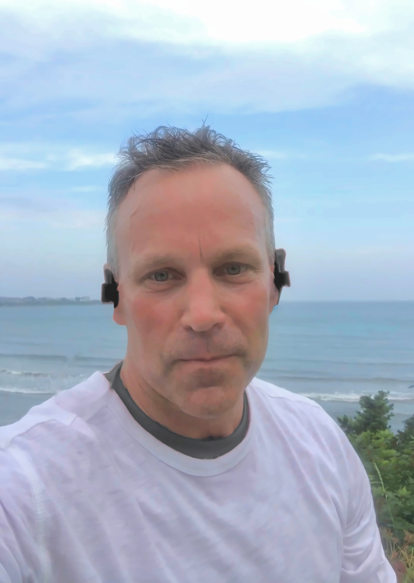 Paul Harkins on the beach wearing headphones with the ocean behind him