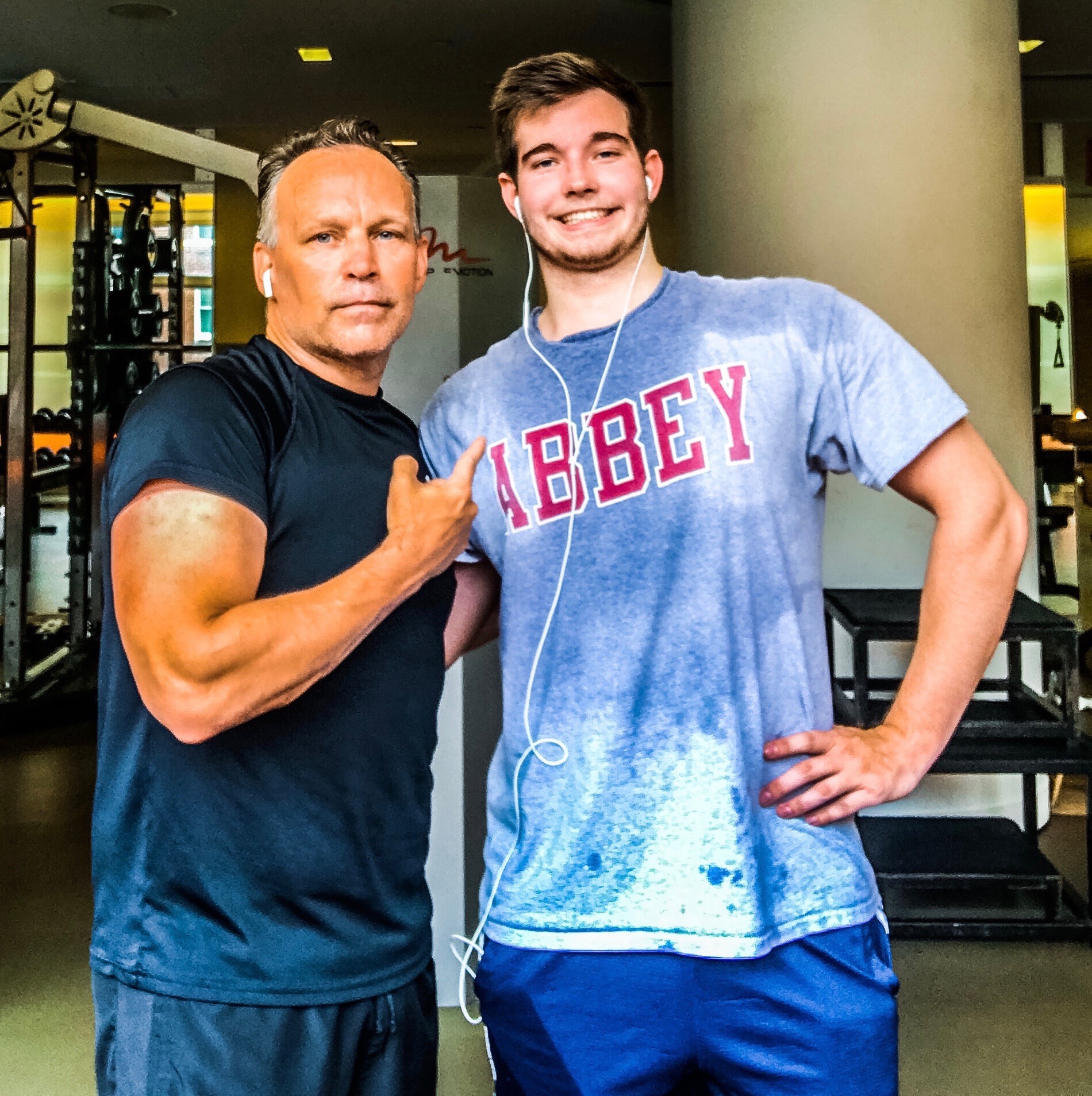 Paul Harkins and his son Scott standing together in a gym, Scott in a grey Abbey t-shirt with earphones