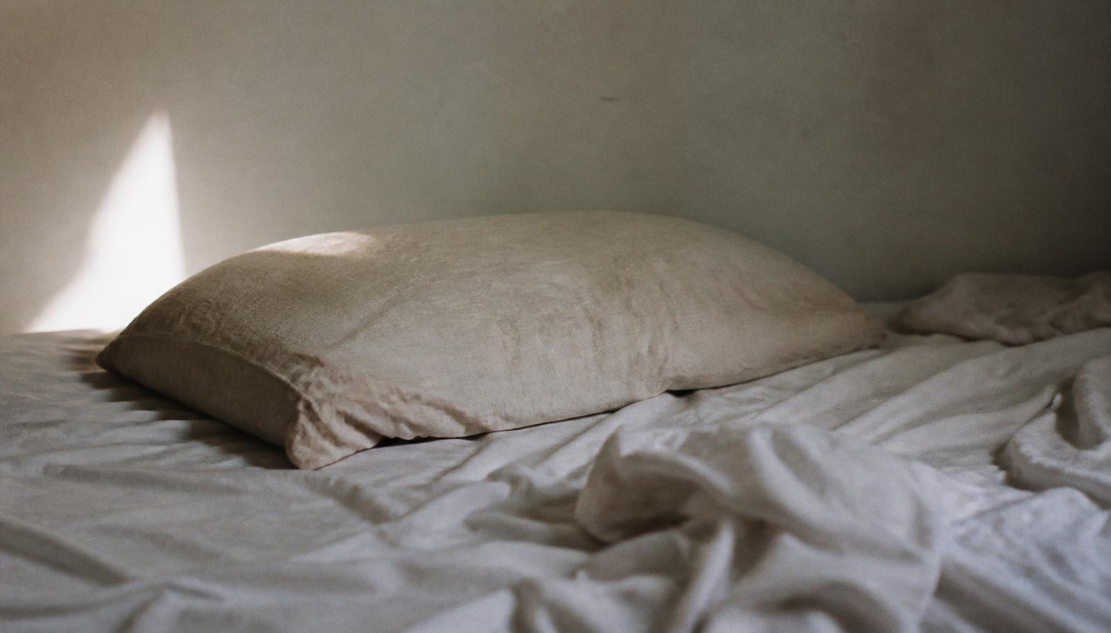 A single worn pillow on an unmade bed in morning light